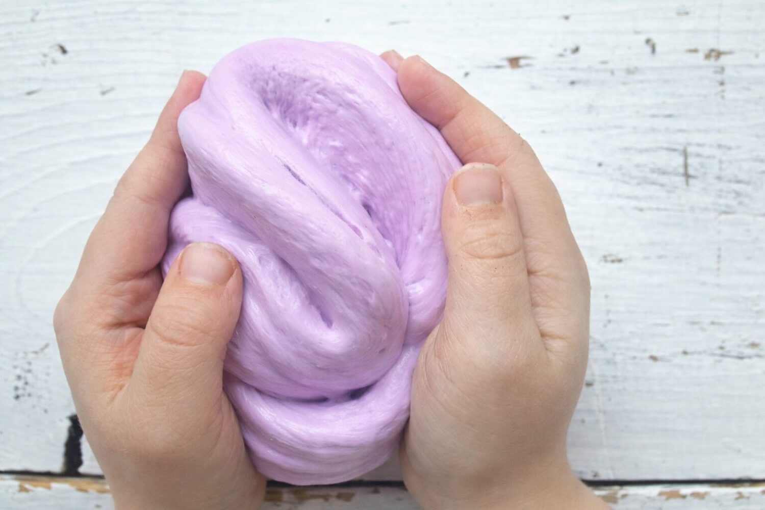 Mains d'enfant étirant une glu aérienne (fluffy slime) rose et élastique.