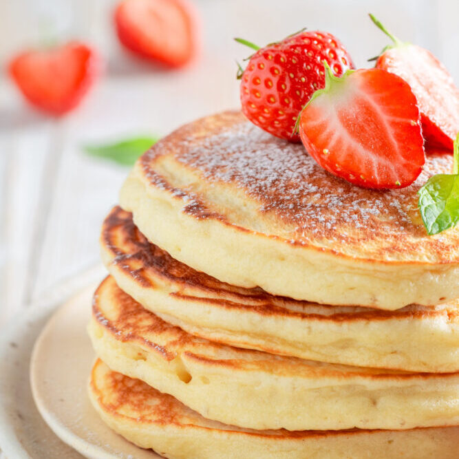 pancakes nature dans une assiette avec quelques fraises sur le dessus